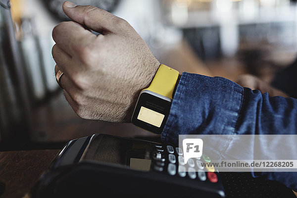 Cropped image of customer doing contactless payment through smart watch at bar counter