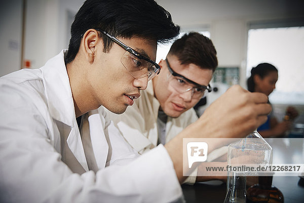 Junge männliche Studenten beim Mischen von Lösungen in Glaswaren im Chemielabor