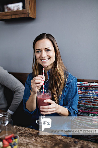 Portrait of smiling young customer having drink while sitting at dining table in restaurant