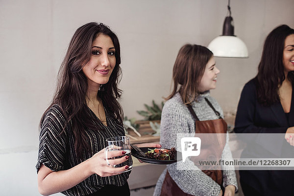 Porträt einer lächelnden jungen Frau mit Essen und Trinken im Stehen mit den Kollegen in der Werkstatt.