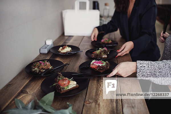 Midsection of female colleagues standing with food plates at table in workshop