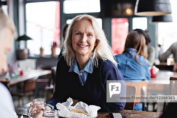 Portrait einer lächelnden reifen Frau  die mit einem Mann am Esstisch im Restaurant sitzt.