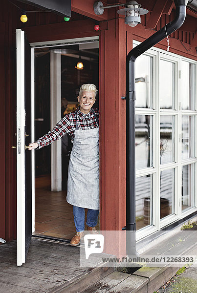 Portrait of happy confident female worker standing at doorway by restaurant
