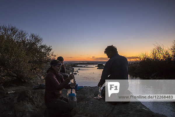 Drei Wanderer ruhen sich aus und füllen Wasser in einem der vielen Bäche entlang des Lost Coast Trail in der violetten Abenddämmerung auf  Kalifornien  USA