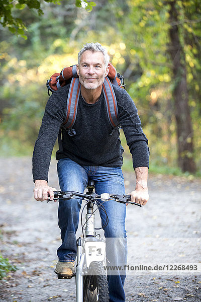 Gray-haired man smiling while riding bicycle in forest  Massachusetts  USA