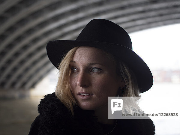 Portrait of blonde woman in black hat below bridge