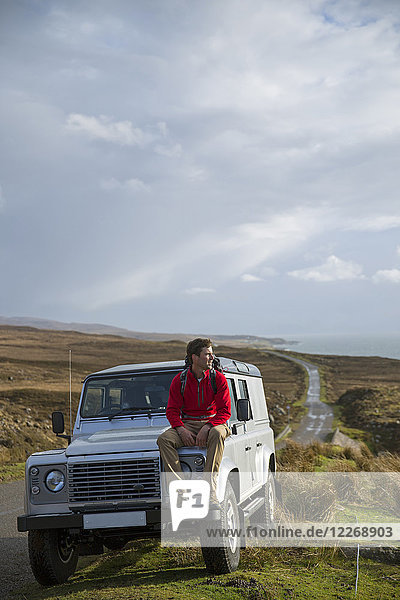 Rucksacktourist auf der Motorhaube eines Geländewagens sitzend  Torridon  Schottland  UK