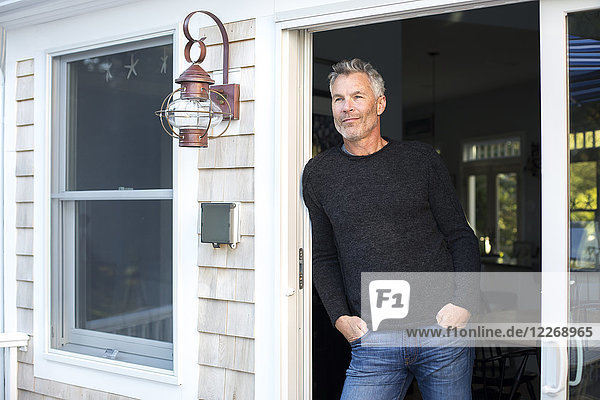 Grauhaariger Mann lehnt mit den Händen in den Taschen am Balkontürrahmen  Massachusetts  USA