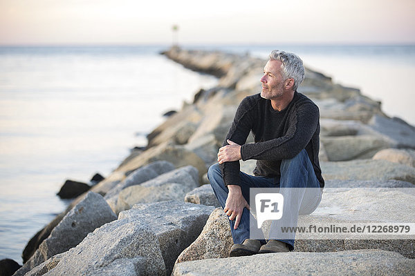 Grauhaariger Mann  der in der Abenddämmerung auf einem Felsen an der Küste nachdenkt  Dennis  Massachusetts  USA