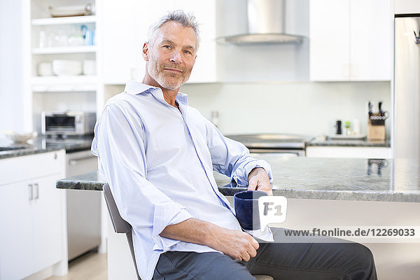 Portrait of gray-haired man holding mug and leaning on kitchen counter  Massachusetts  USA