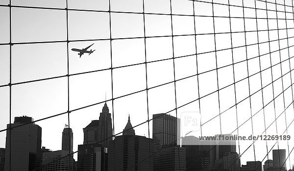 Skyline von Manhattan von der Brooklyn Bridge aus gesehen  Wolkenkratzer  Passagierflugzeug am Himmel  New York  USA.