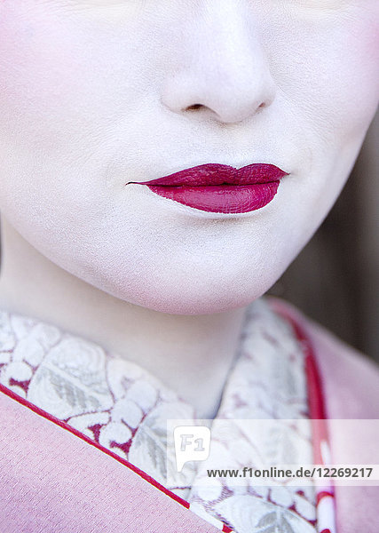 Nahaufnahme von Geishas Gesicht mit traditionellem Make-up  blassweißer Haut und leuchtend rosa Lippenstift.
