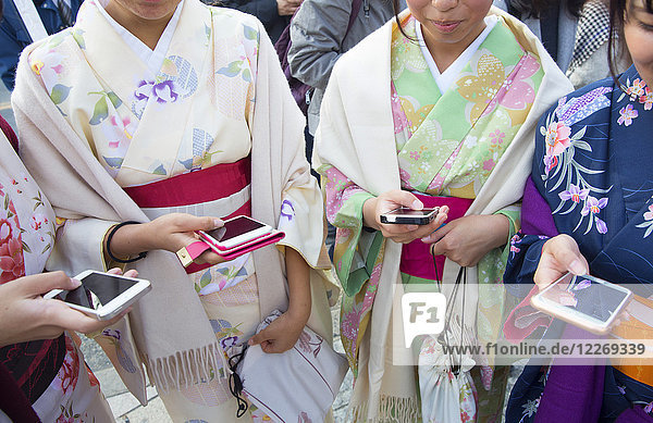 Nahaufnahme einer Gruppe von Frauen in traditionellen japanischen Kimonos  die Seite an Seite stehen und Smartphones halten.