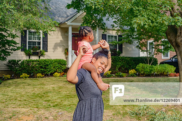 Mid adult woman in garden carrying baby daughter on shoulders portrait