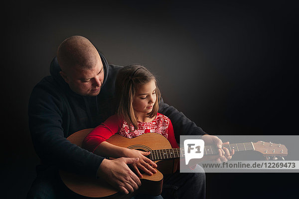 Father teaching daughter to play guitar