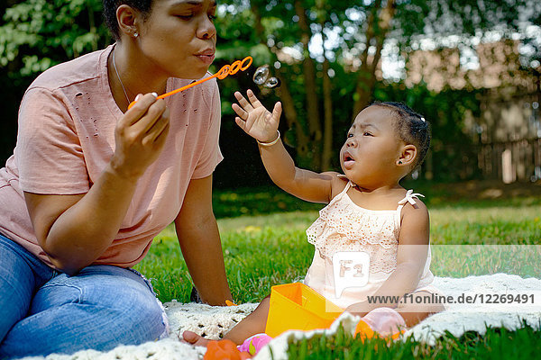 Mittelgroße erwachsene Frau bläst Blasen im Garten für ihre kleine Tochter