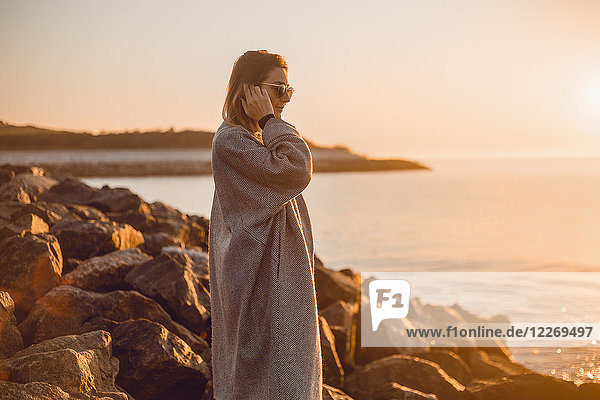 Porträt einer Frau mit Sonnenbrille und Wintermantel auf Felsen stehend und aufs Meer blickend  Odessa  Odeska Oblast  Ukraine  Osteuropa