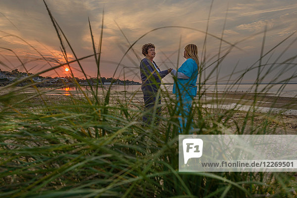 Frau und Pflegerin genießen den Sonnenuntergang am Abend am Meer