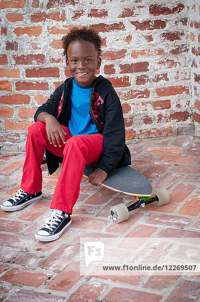 Porträt eines Jungen  der auf einem Skateboard sitzt und lächelt