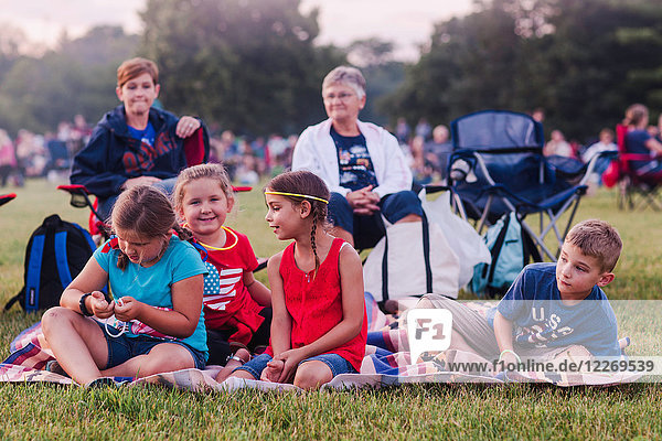 Gruppe von Erwachsenen und Kindern  im Freien sitzend  während der Feierlichkeiten zum 4. Juli