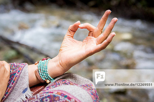 Young woman meditating by river  close up of hand