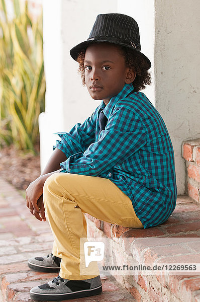 Portrait of young boy  sitting outdoors  wearing fedora