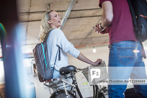 Young woman with bicycle greeting colleague in office