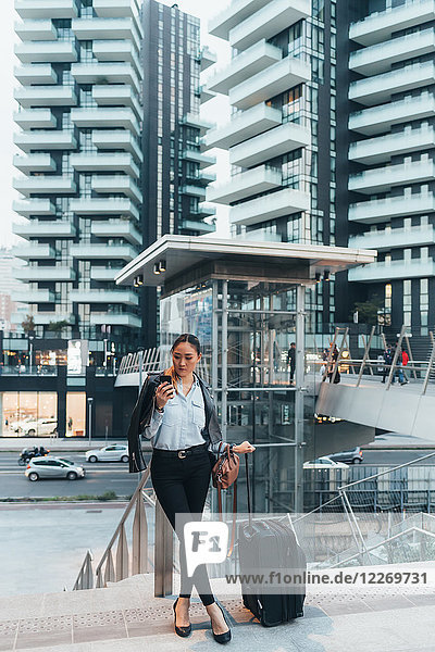 Geschäftsfrau  im Freien  mit Rollkoffer in der Hand  mit Smartphone