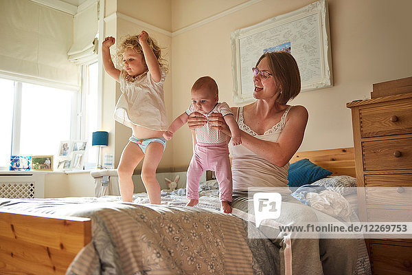 Woman on bed playing with baby and toddler daughters