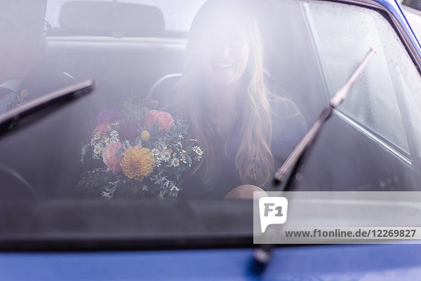 Junge Frau im Auto mit Blumenstrauss  auf dem Weg von der Hochzeit
