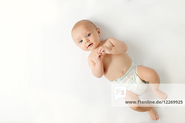Overhead view of baby boy lying on white background looking at camera