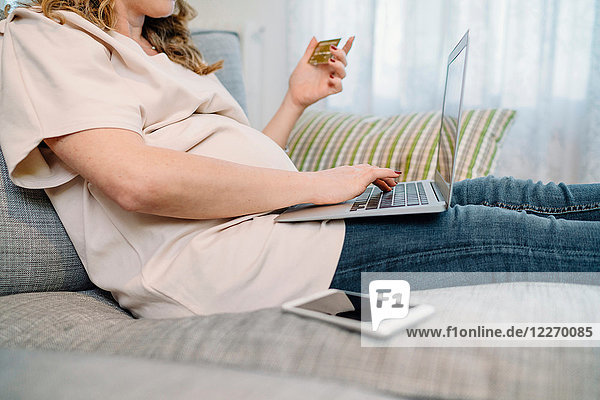 Schwangere Frau auf dem Sofa  die mit dem Laptop online einkauft  beschnitten