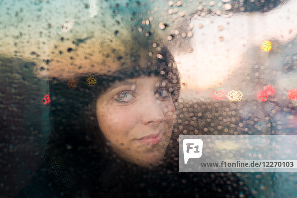 Frau schaut aus dem regennassen Fenster