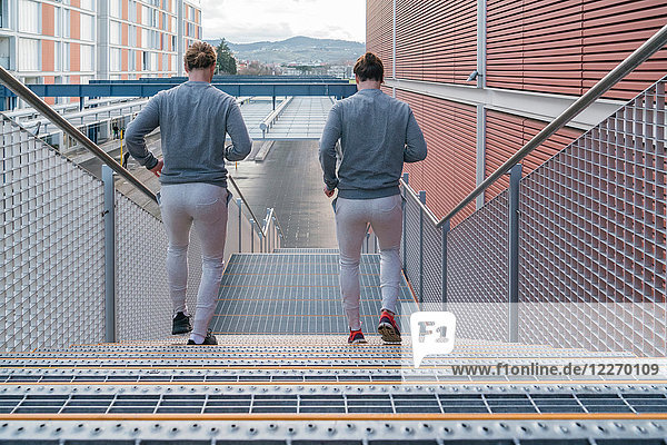 Junge erwachsene männliche Zwillinge laufen zusammen  laufen die Stadttreppe hinunter  Rückansicht