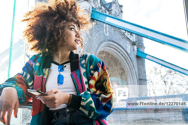 Young girl outdoors  holding smartphone  looking away  Tower Bridge in background  London  England  UK