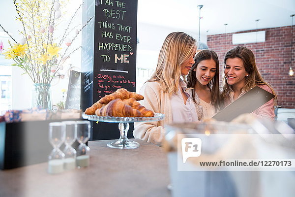 Drei Freundinnen  die sich die Speisekarte im Café ansehen