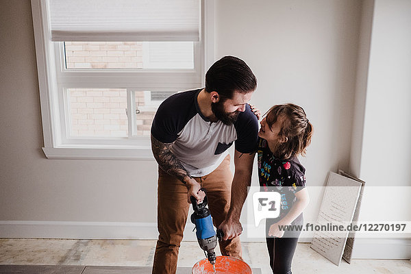 Father and daughter mixing cement in bucket with hand mixer