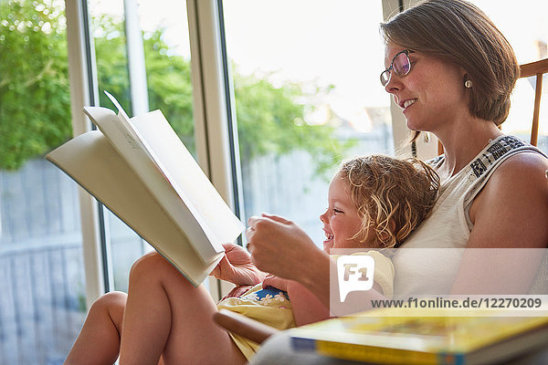 Mutter und Kleinkind Tochter lesen an der Terrassentür
