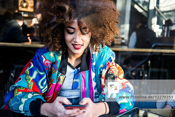 Young girl sitting in bar  using smartphone  view through window  London  England  UK