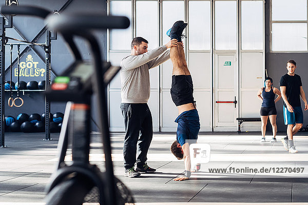 Man in gym helping friend do handstand