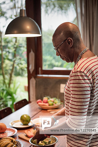 Reifer Mann am Küchentisch beim Zubereiten von Obst in der Schüssel