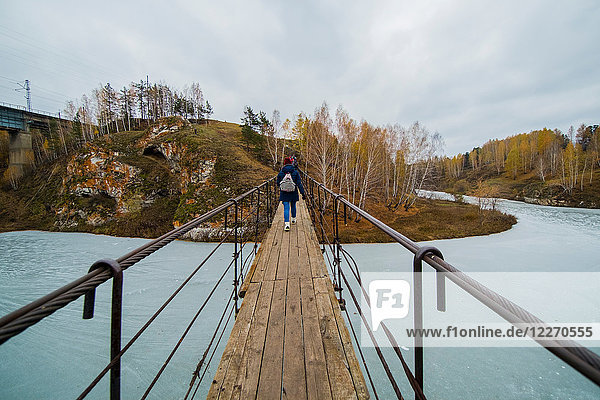Rear view of small group of hikers walking over river footbridge  Kislokan  Evenk  Russia