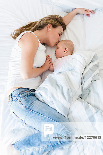 Mutter küsst schlafendes Baby im Bett