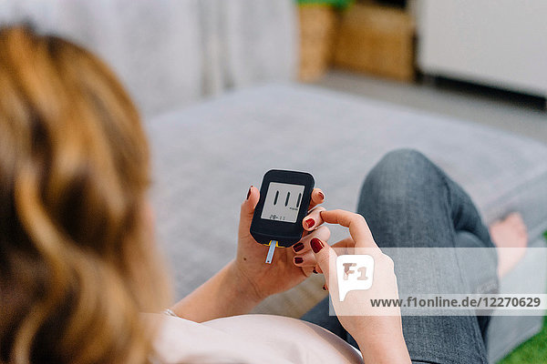 Pregnant woman on sofa looking at blood sugar test  over shoulder view