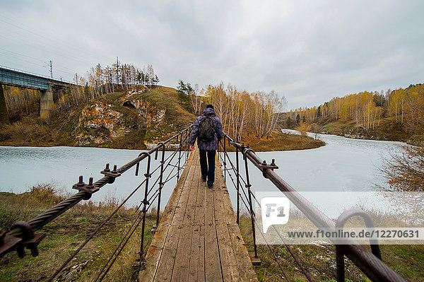 Rear view of young male hiker walking over river footbridge  Kislokan  Evenk  Russia