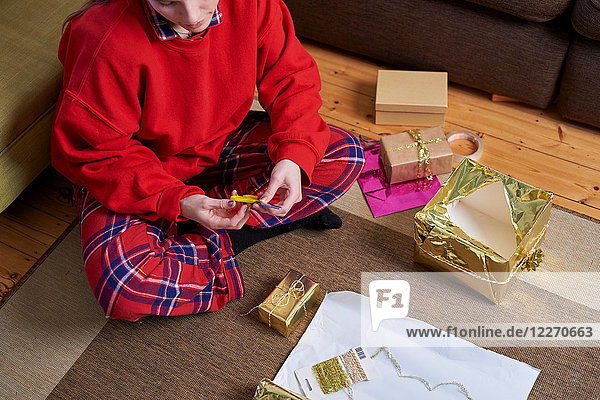 Junge Frau sitzt auf dem Wohnboden und packt Geschenke ein  Draufsicht