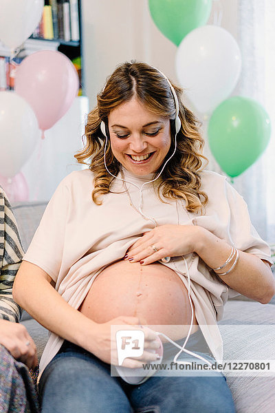 Pregnant woman on sofa using prenatal listening device