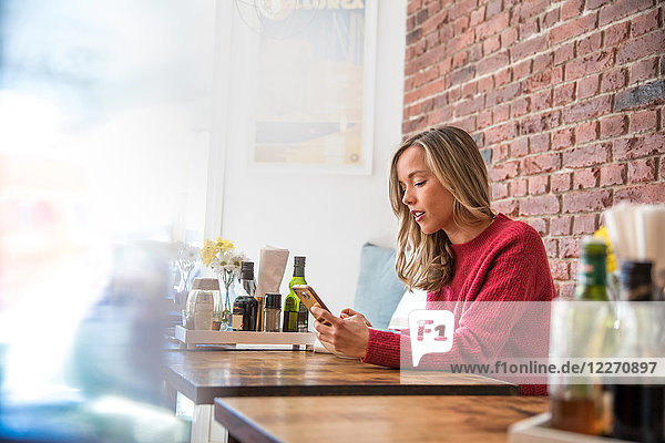 Frau sitzt im Café und schaut auf ihr Smartphone