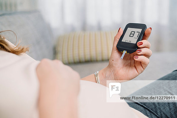 Pregnant woman on sofa looking at blood sugar test  cropped