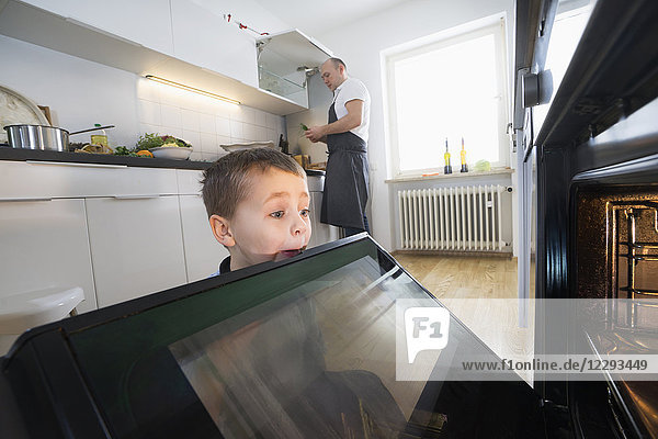 Vater kocht Essen  während hungriger kleiner Junge in den Ofen schaut